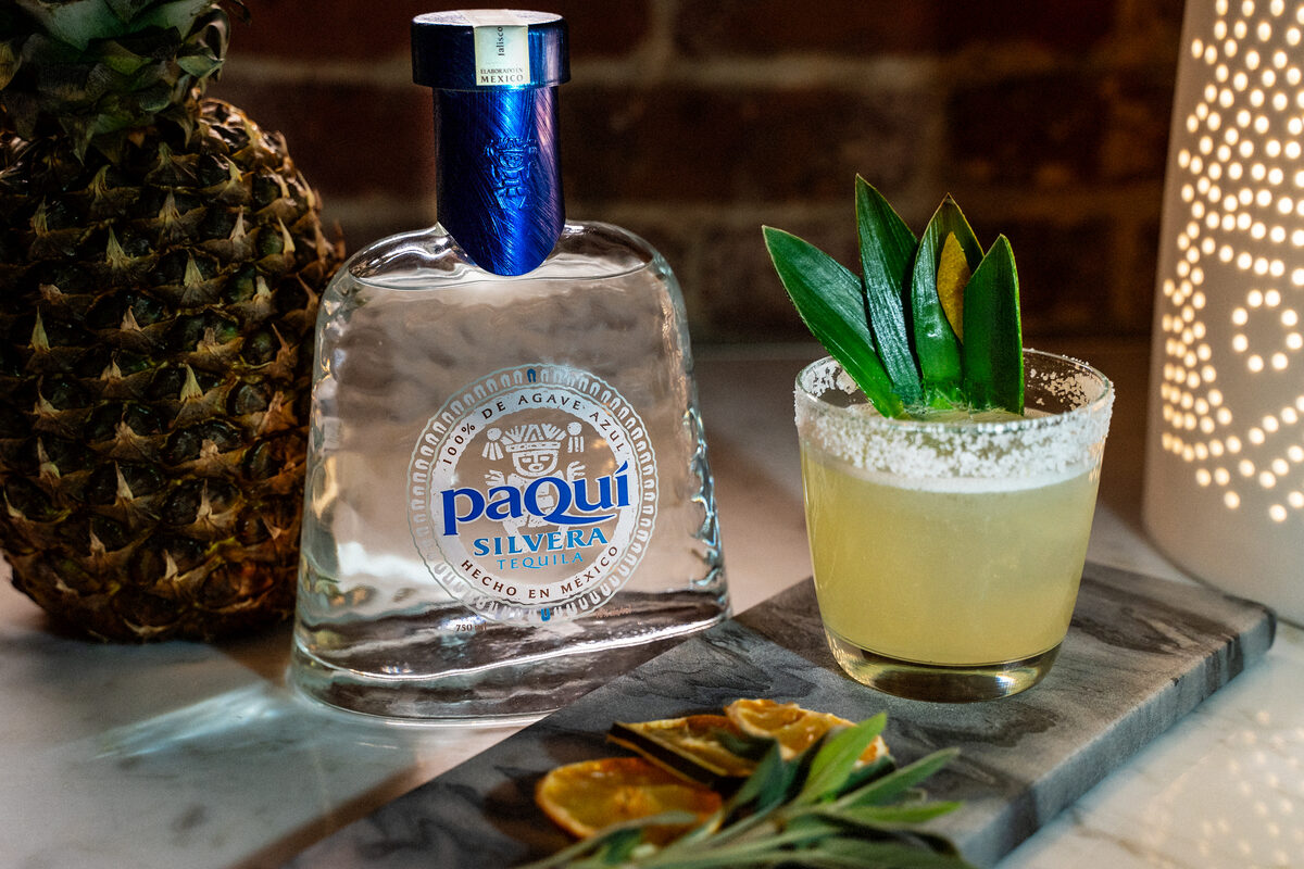 PaQui Tequila bottle with pineapple and cocktail in bar setting