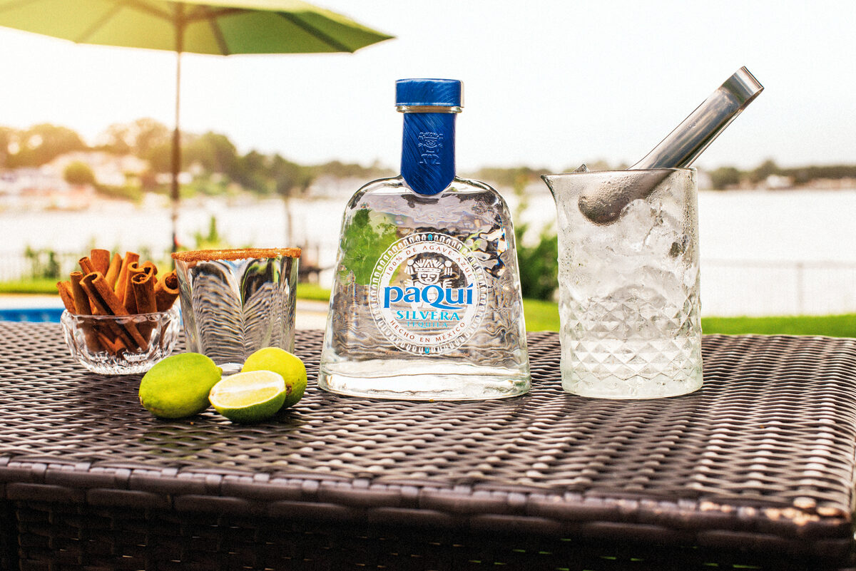 PaQui Silvera Tequila bottle with limes, cinnamon sticks, and ice bucket on poolside table