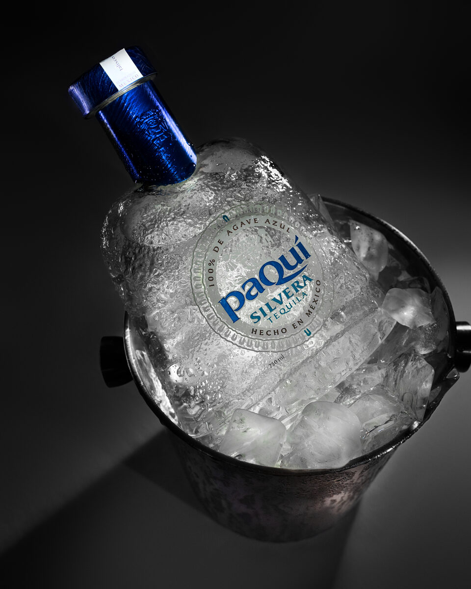 PaQui Silvera Tequila bottle nestled in ice bucket, dramatic studio lighting